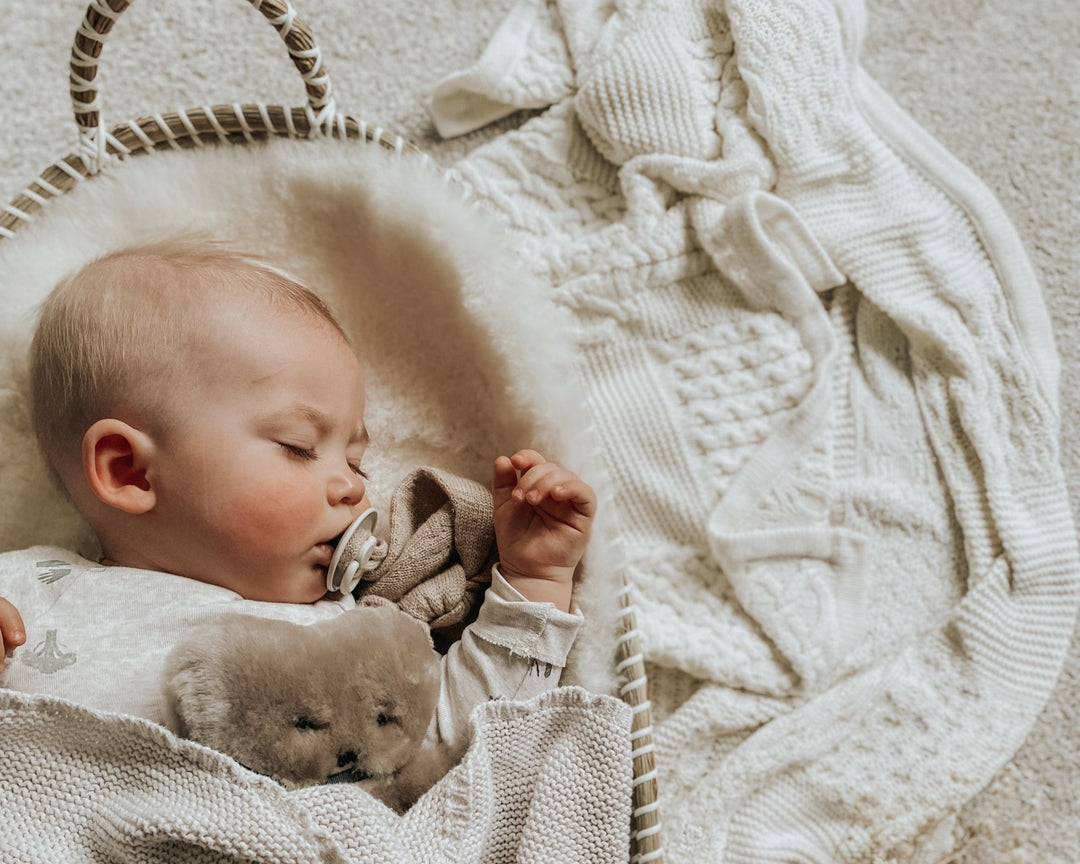 A baby sleeping on a premium sheepskin liner holding a latte coloured flatout bear