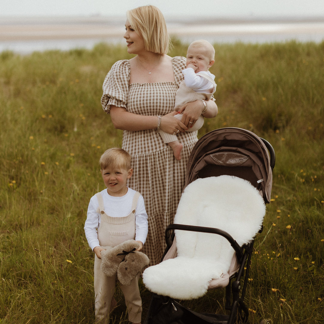 Sheepskin pram snuggler in pale white gender neutral shade in a joolz aer pram with a mum and baby next to it