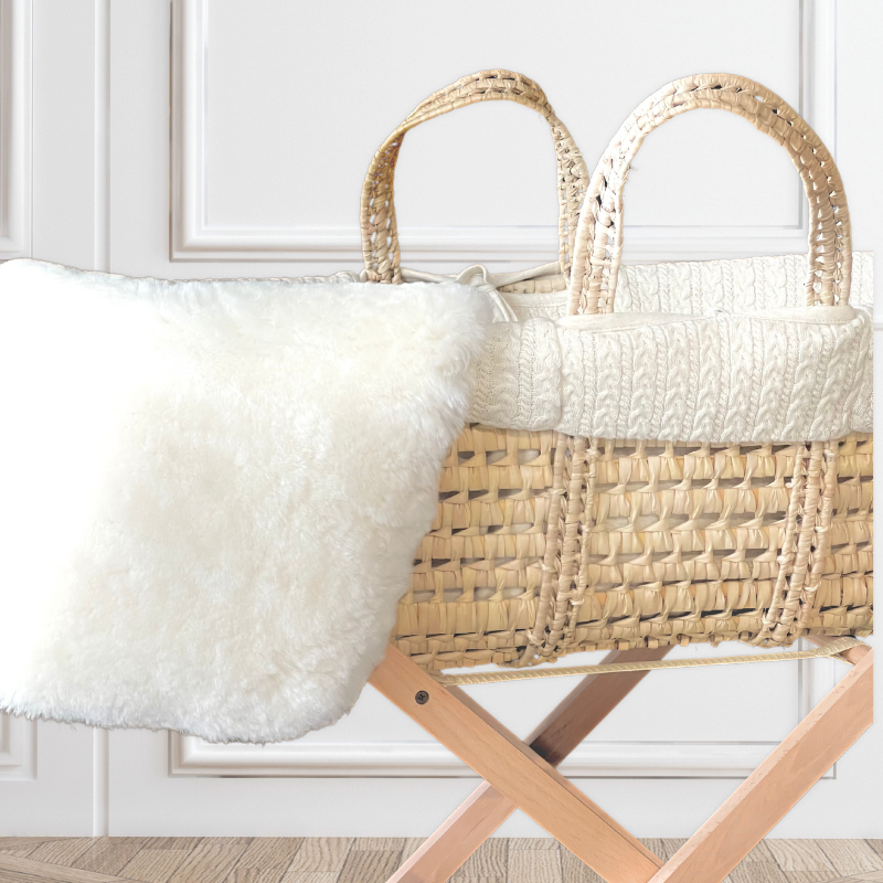 Baa Baby sheepskin bassinet liner in white hanging over the side of a natural moses basket which it also fits