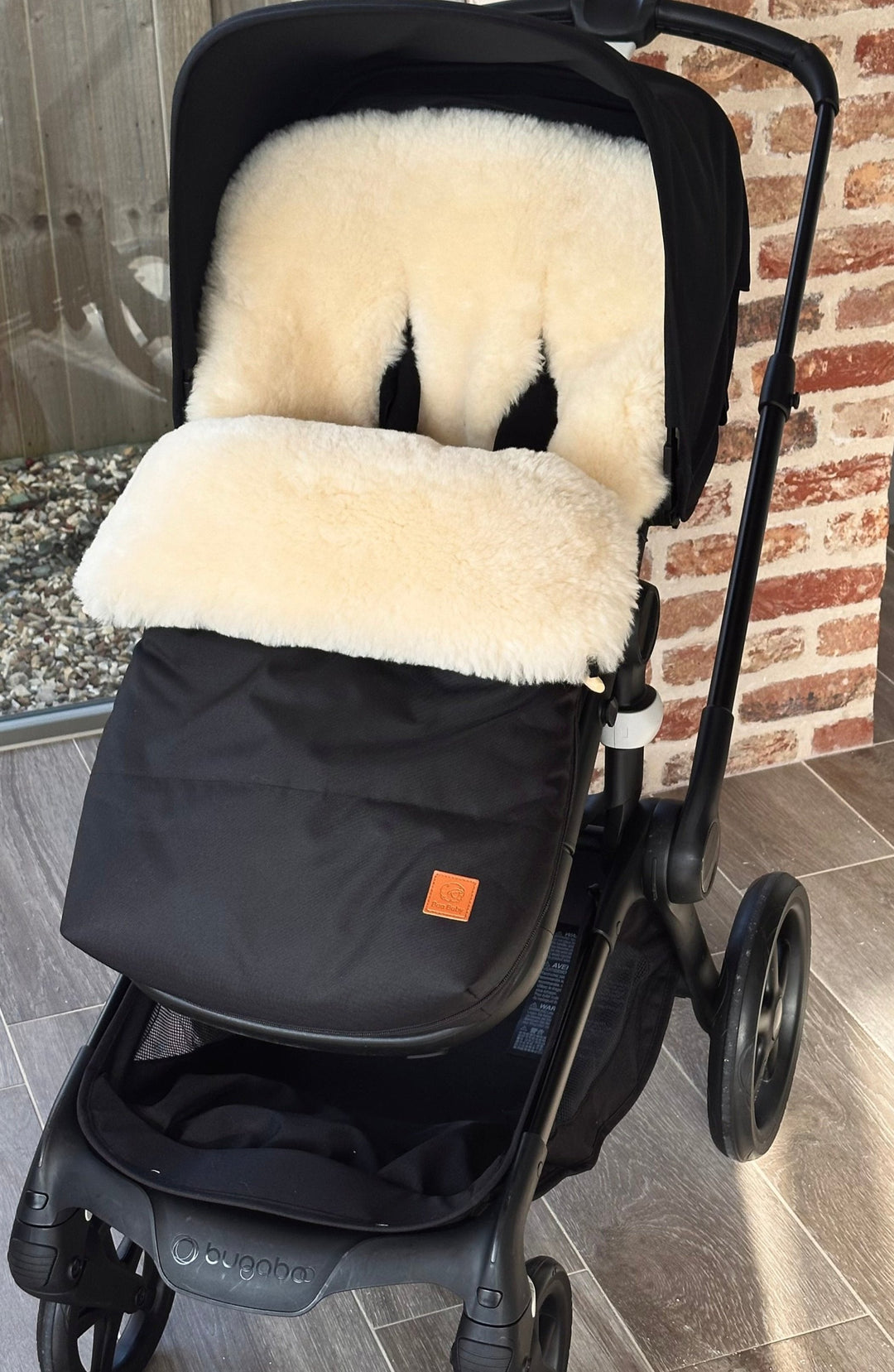 Luxury sheepskin footmuff with milk shade lambskin and black outer shown in a bugaboo fox pram