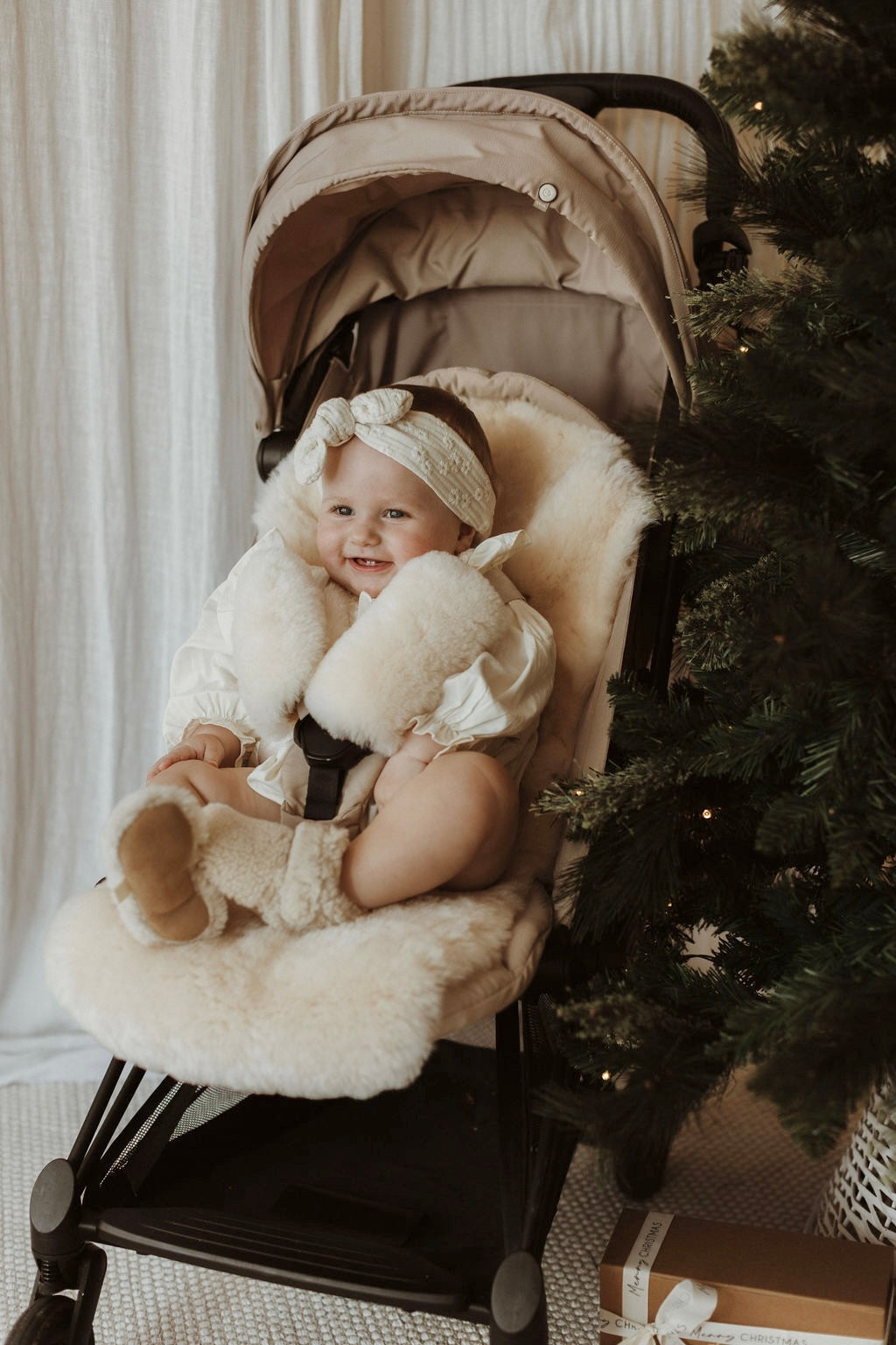 Baby looking cosy in a babyzen yoyo pram with additional cushioning of a sheepskin pram liner in neutral milk and pram harness strap covers