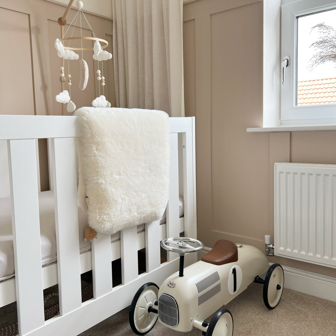 White sheepskin cot liner hanging over a toddler bed in a newborn baby nursery in neutral shades