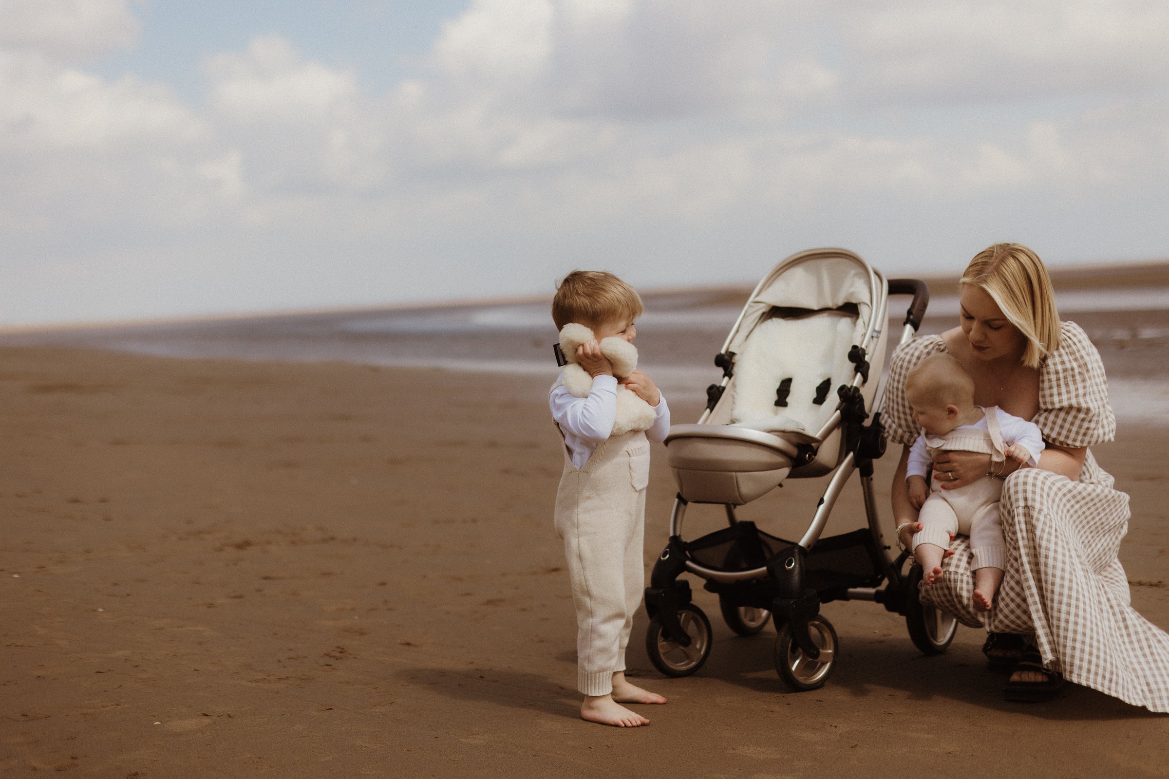 Sheepskin liner milk in a neutral pram with baby on holiday, older child holding a flat teddy bear