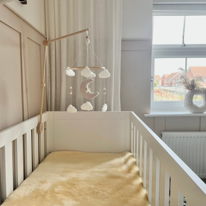 Heitmann Felle Sheepskin cot topper and liner for a baby crib shown in a white cot in a neutral nursery