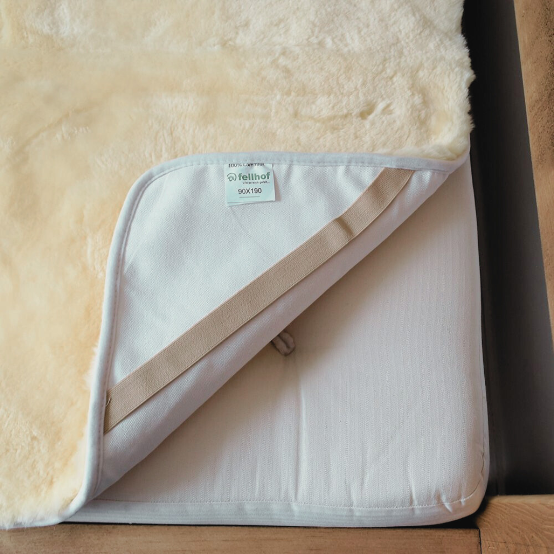 Sheepskin cot bed liner for a baby or toddler to help them sleep, showing how this Fellhof medical sheepskin attaches to the  bed