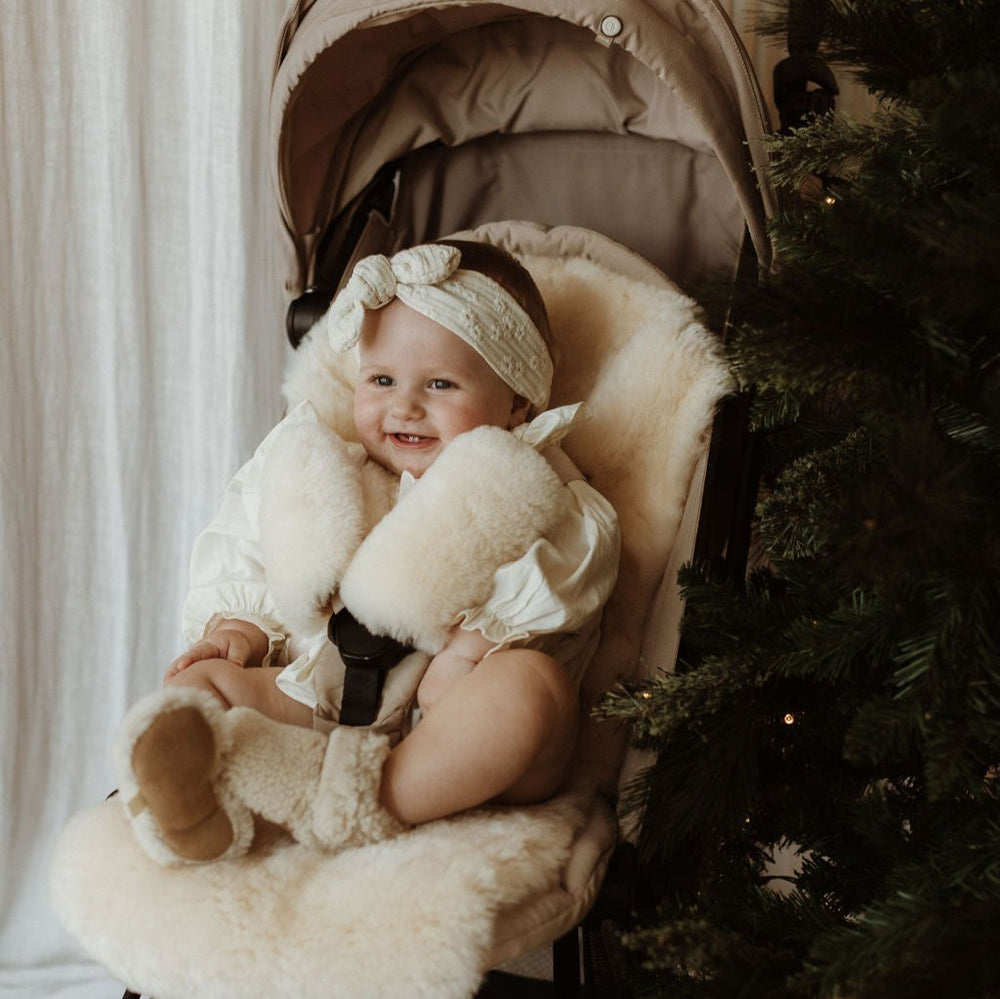 Sheepskin baby gifts showing a milk pram liner in a babyzen yoyo and harness strap covers.  Baby has merino boucle booties on showing ideal toddler Christmas gift ideas