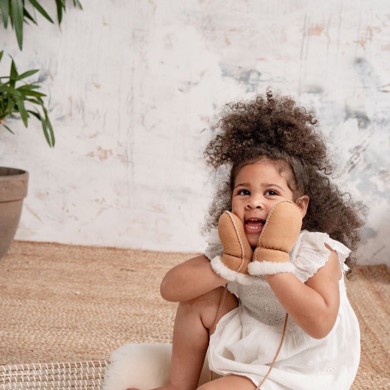 Toddler smiling wearing neutral mittens on string